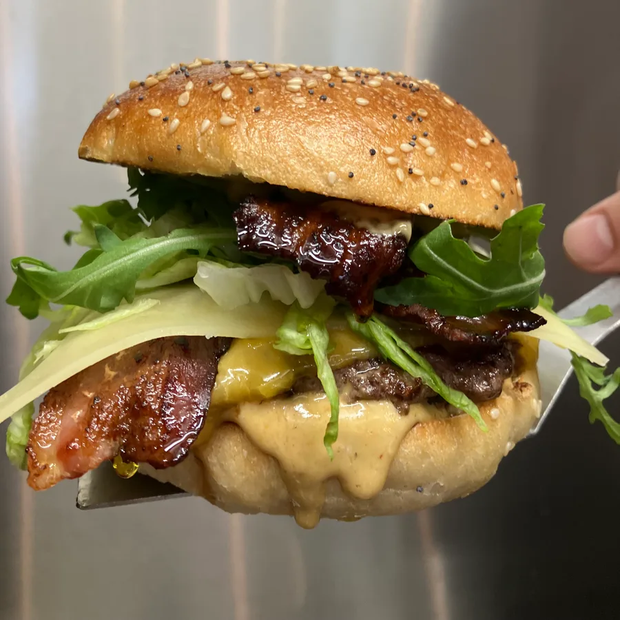Burger bacon et cheddar fondu présenté sur la spatule en cuisine — Pipok